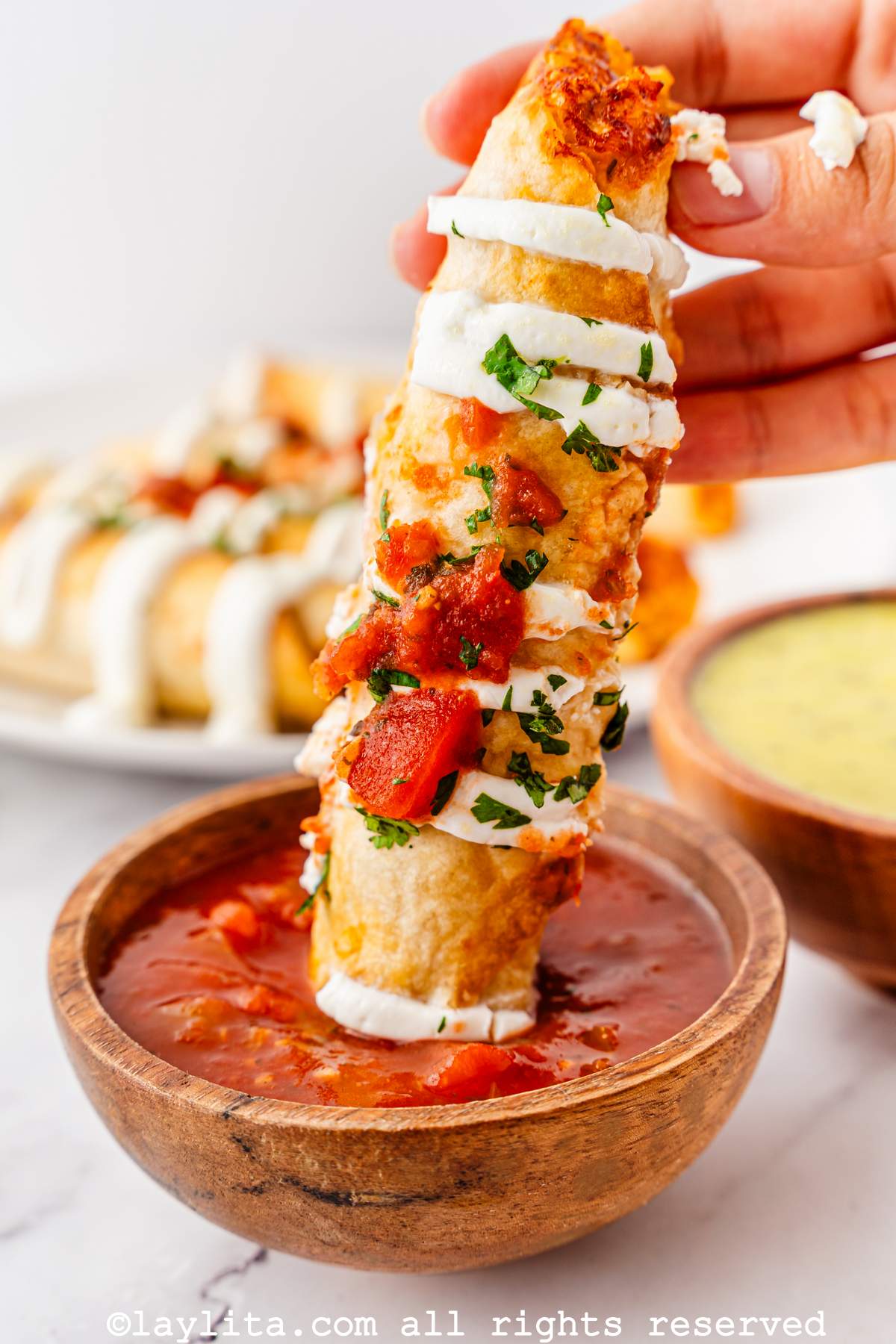 A crispy flauta or taquito being dipped into a bowl of red salsa