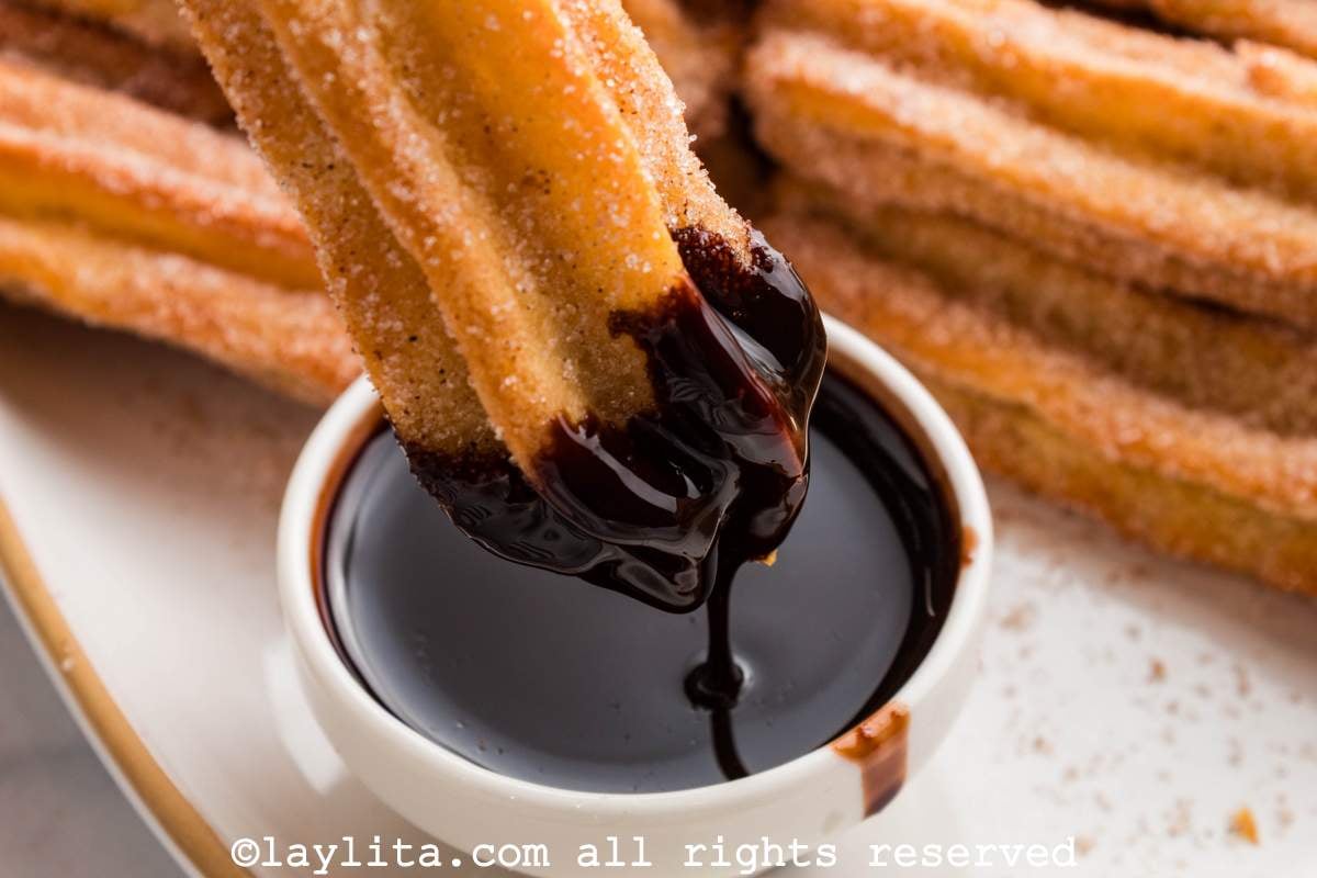 Close up of a churro being dipped into a bowl of chocolate sauce