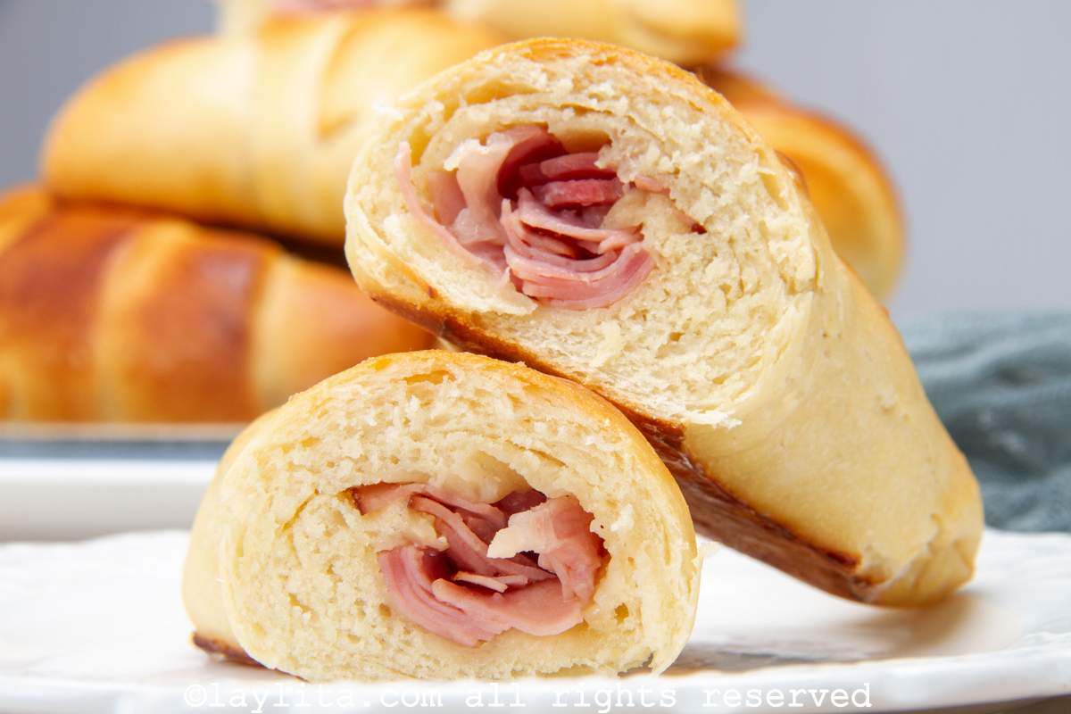 Closeup of a ham cachito bread roll cut in half with the halves leaning on each other to show the ham filling