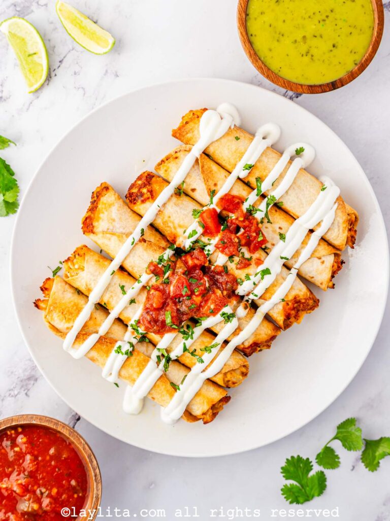Overhead shot of air fryer chicken taquitos on a white plate with sour cream and salsa on top