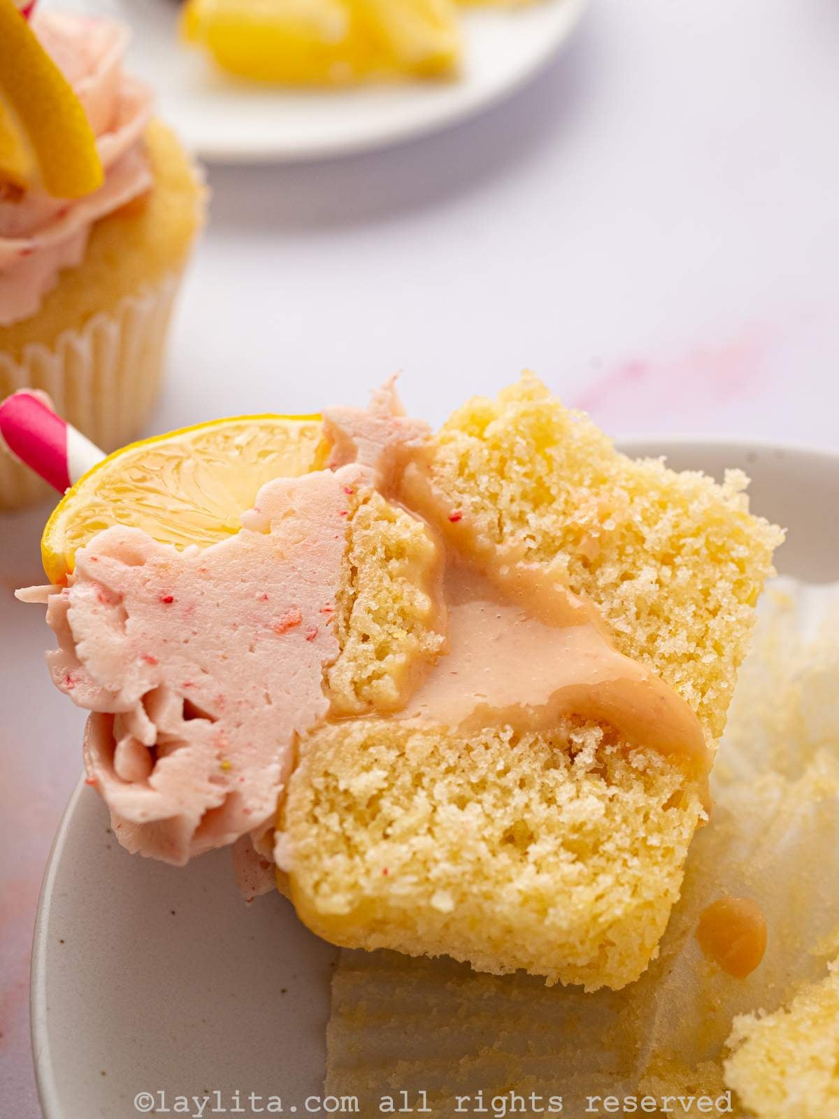 A cupcake filled with a strawberry lemon curd cut in half, with the filling oozing out