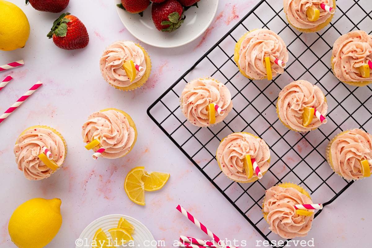 Overhead view of several cupcakes decorated with strawberry frosting, some are on a wire rack and other are on the kitchen counter