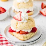 Two plates of strawberry shortcakes lined up, both garnished with strawberries and cream., with additional strawberries on the side