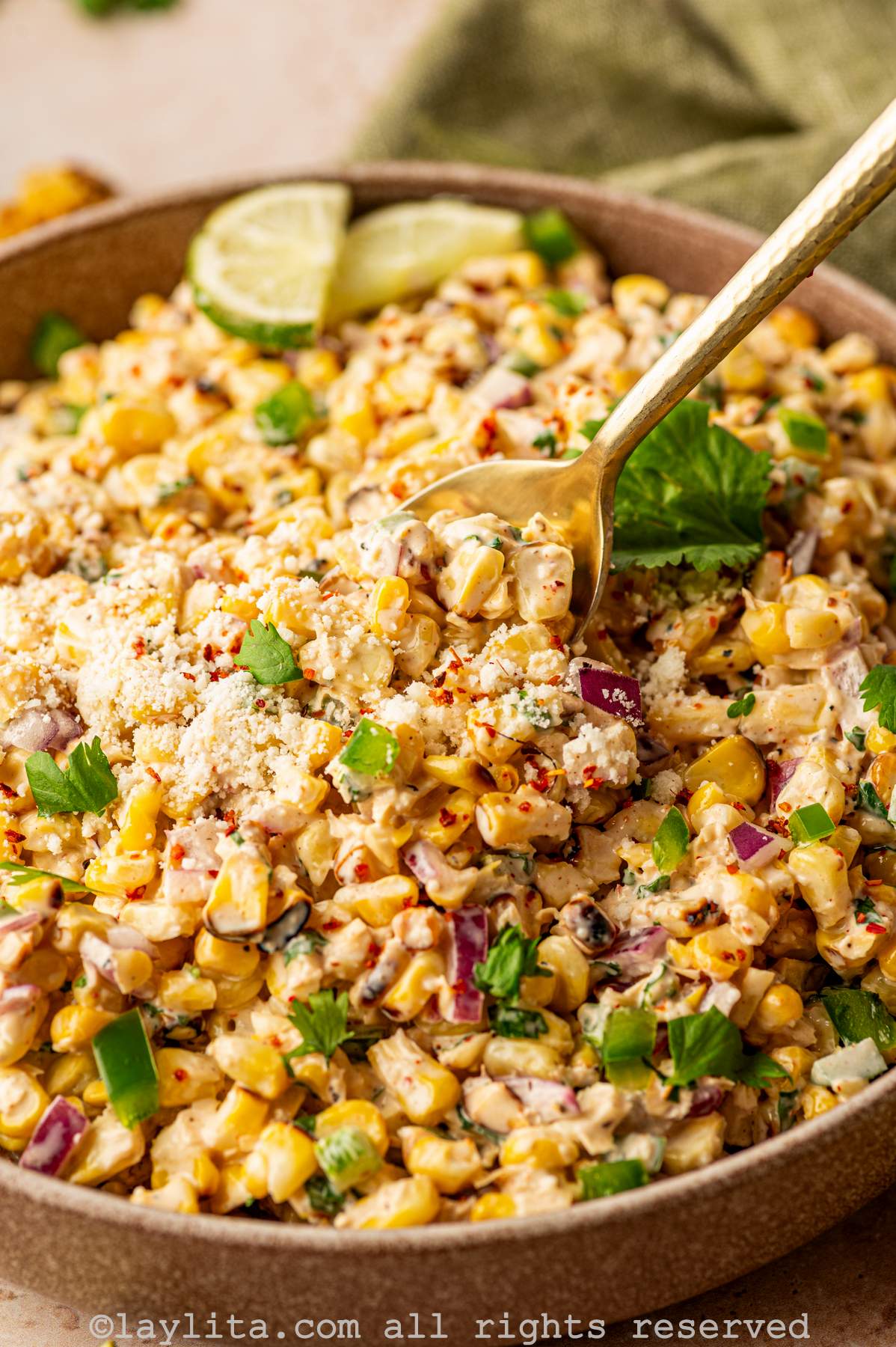 Closeup view of Mexican street corn salad topped with cilantro and cotija cheese, with a spoon inside the bowl