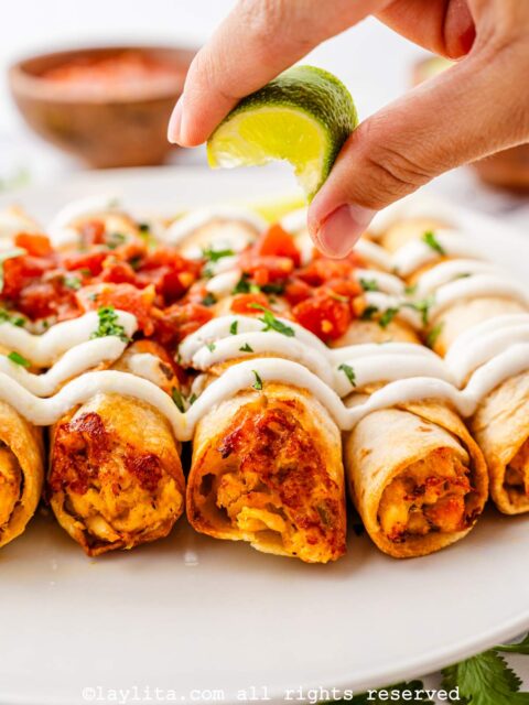 Hand squeezing lime on top of a plate of air fryer chicken flautas or taquitos
