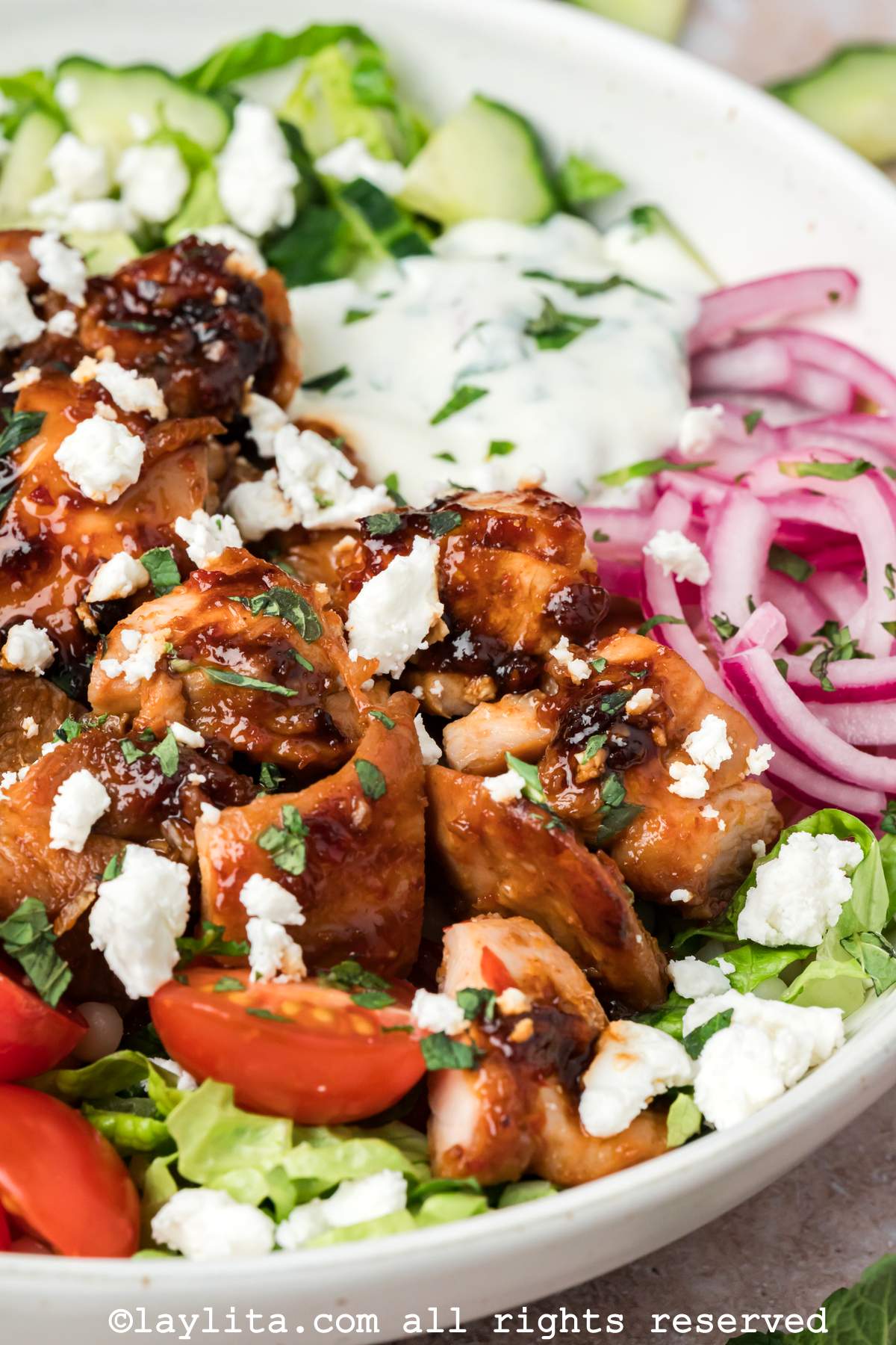 Side view of harissa chicken bowl with couscous, vegetables and mint yogurt sauce