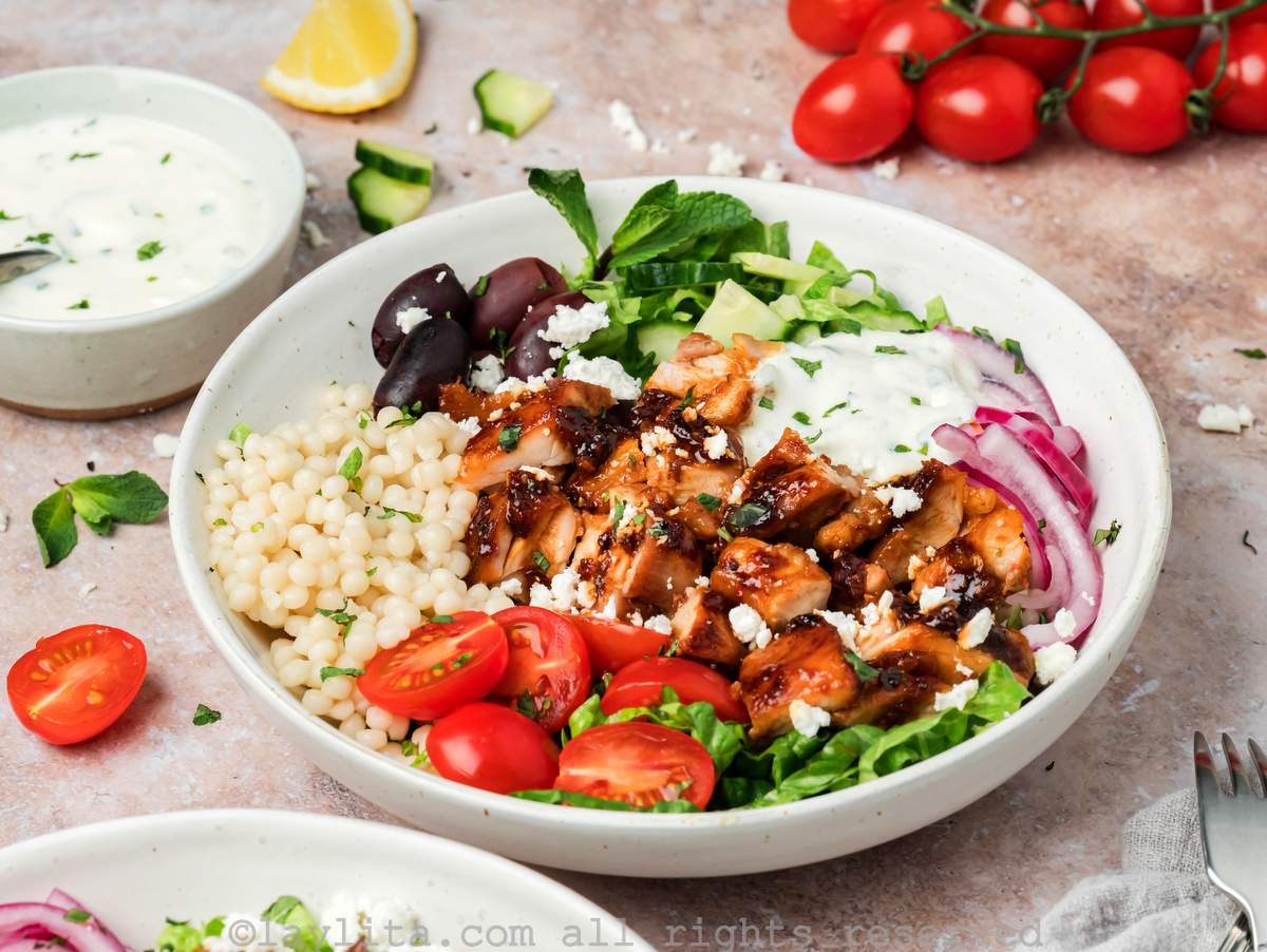 A harissa chicken bowl with vegetable toppings and mint yogurt sauce on top.
