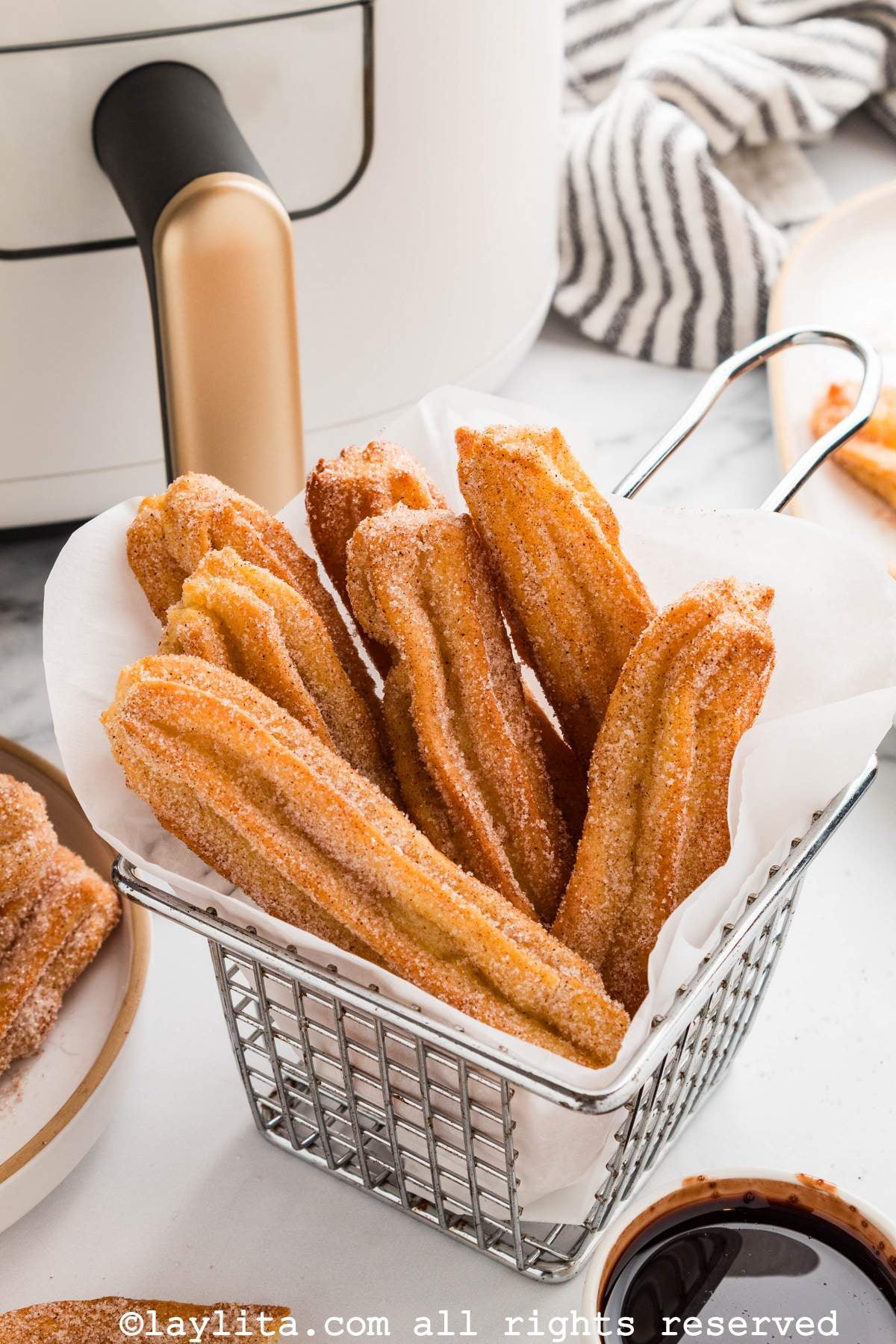 Several churros served in a small fryer basket with a white air fryer in the background