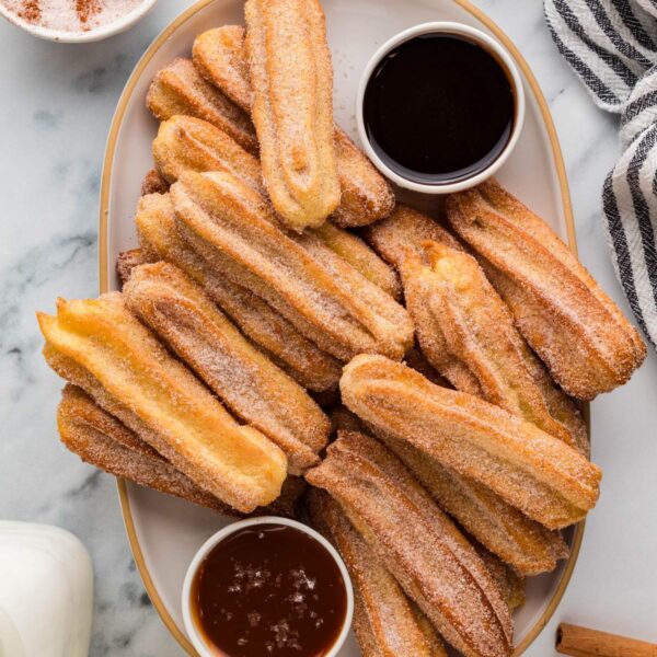 Overhead view of several churros on a tray with a bowl of chocolate sauce and bowl of caramel, with a striped kitchen towel on the side