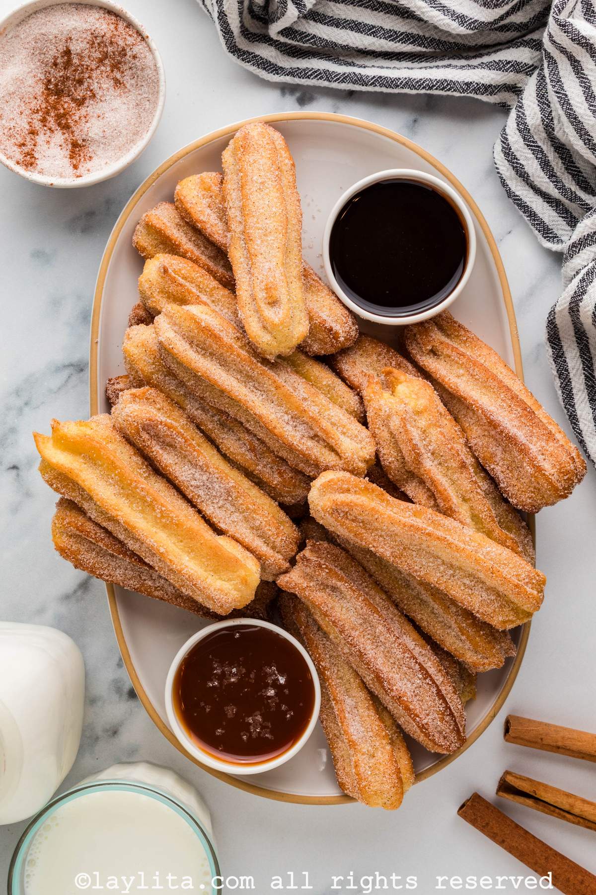 Overhead view of several churros on a tray with a bowl of chocolate sauce and bowl of caramel, with a striped kitchen towel on the side