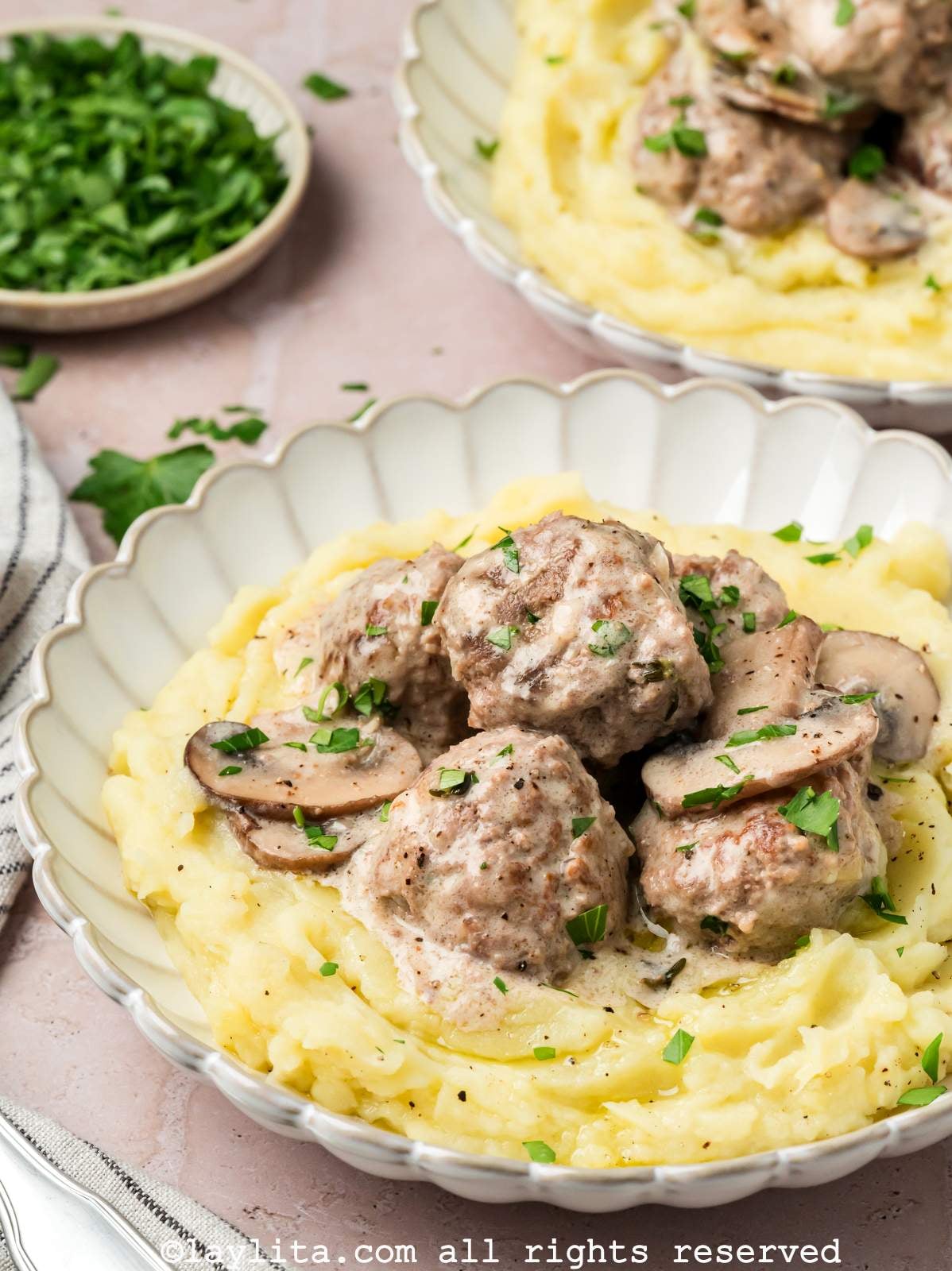 Side view of two plates of mashed potatoes topped with beef meatballs in a stroganoff sauce