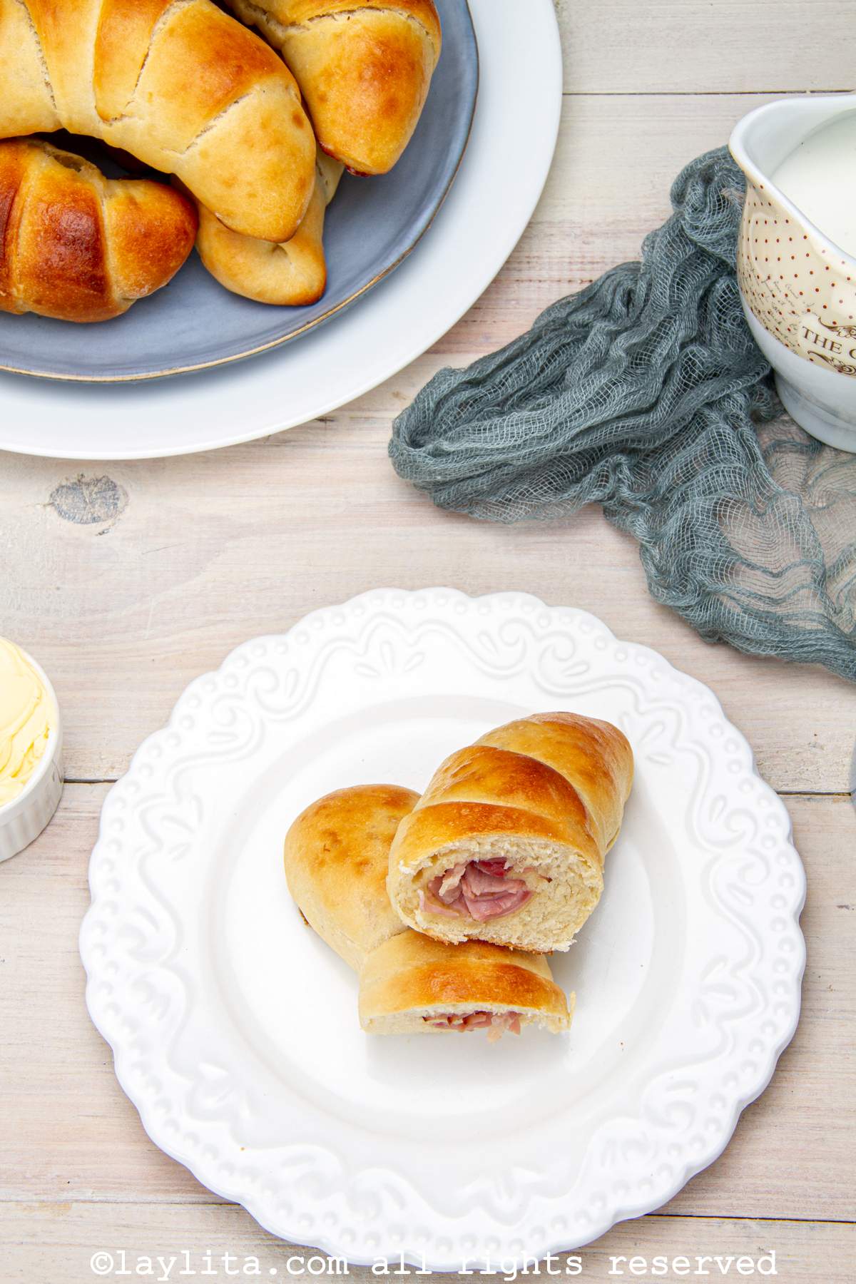 Overhead view of a white plate with a ham stuffed bread roll cut in half, with more bread rolls in the background