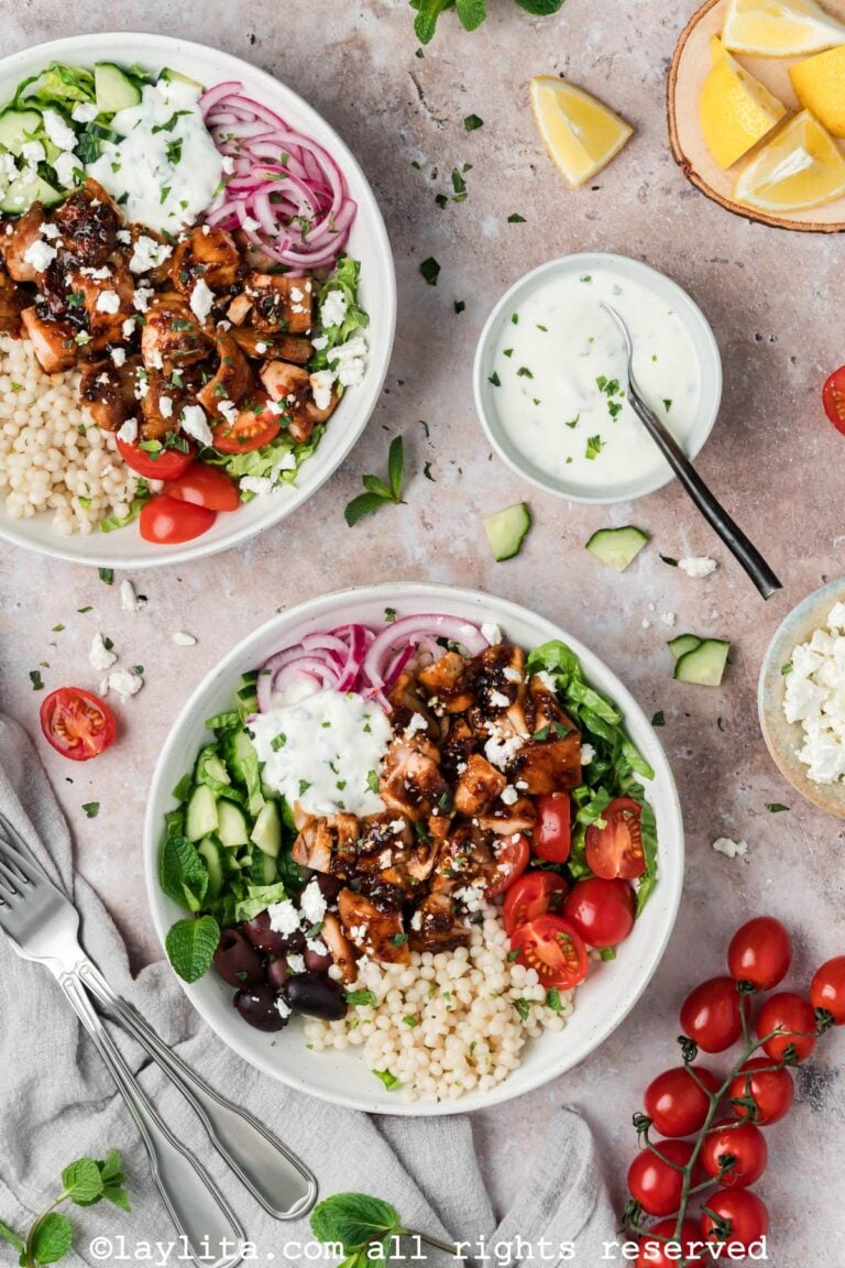 Overhead view of two honey harissa chicken bowls next to a small bowl of mint yogurt sauce.