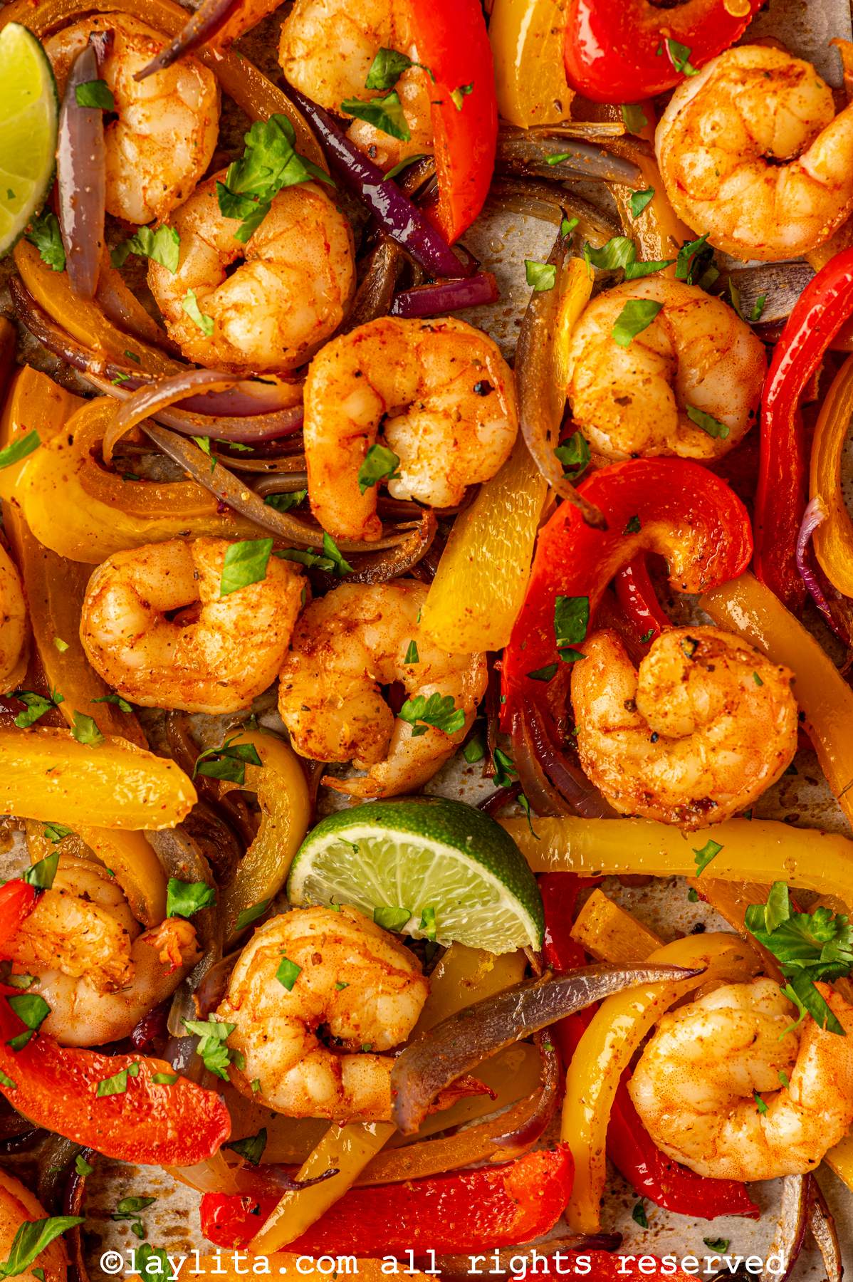 Closeup shot of a roasted Fajita shrimp and sliced roasted peppers and onions on  a baking sheet with lime wedges and chopped cilantro