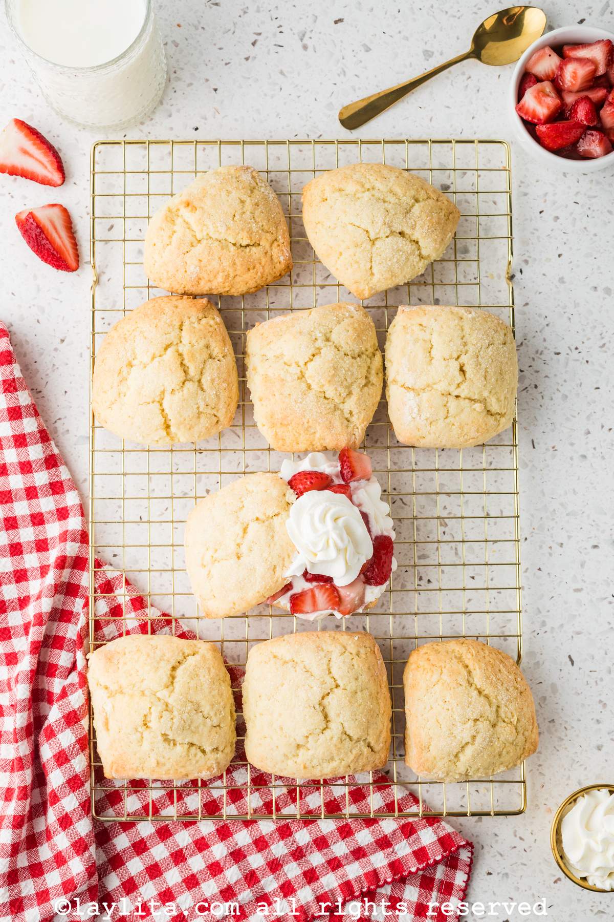 Overhead shot of a baking rack with several shortcake biscuits, with one of them cut in half and topped with strawberries and cream