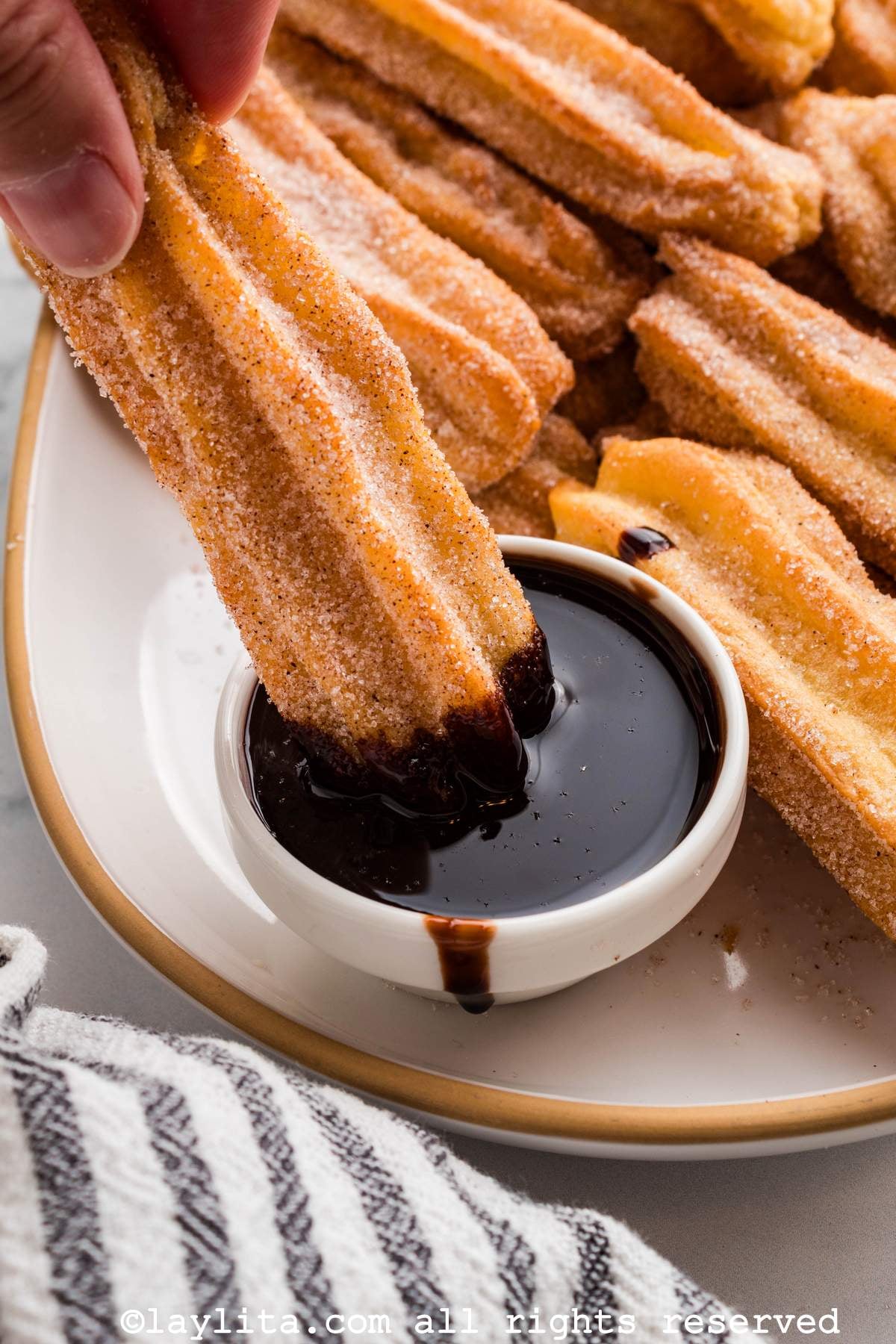 Close up of a tray of churros with one being dipping into a chocolate sauce