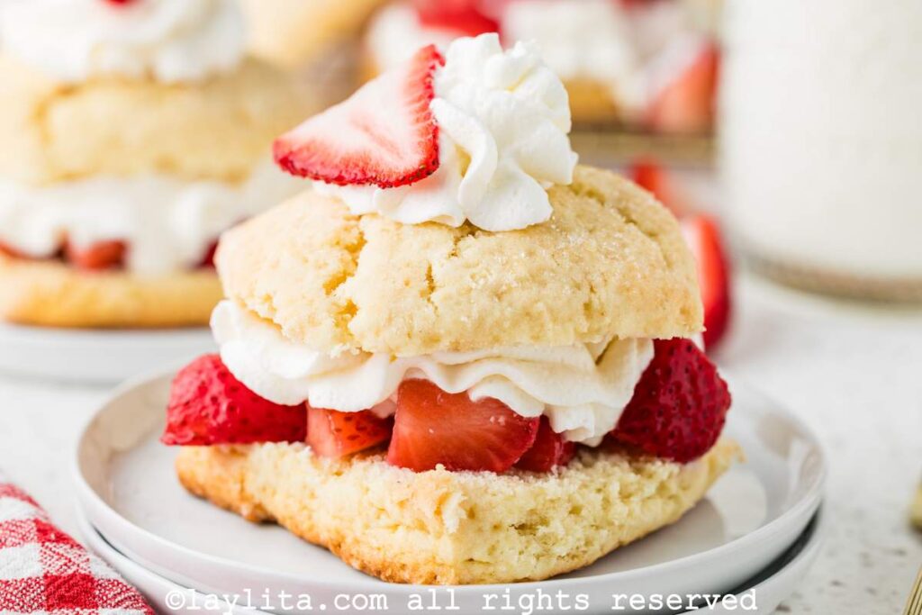 Side view of a strawberry shortcake on a plate with layers of biscuits and strawberries and cream.