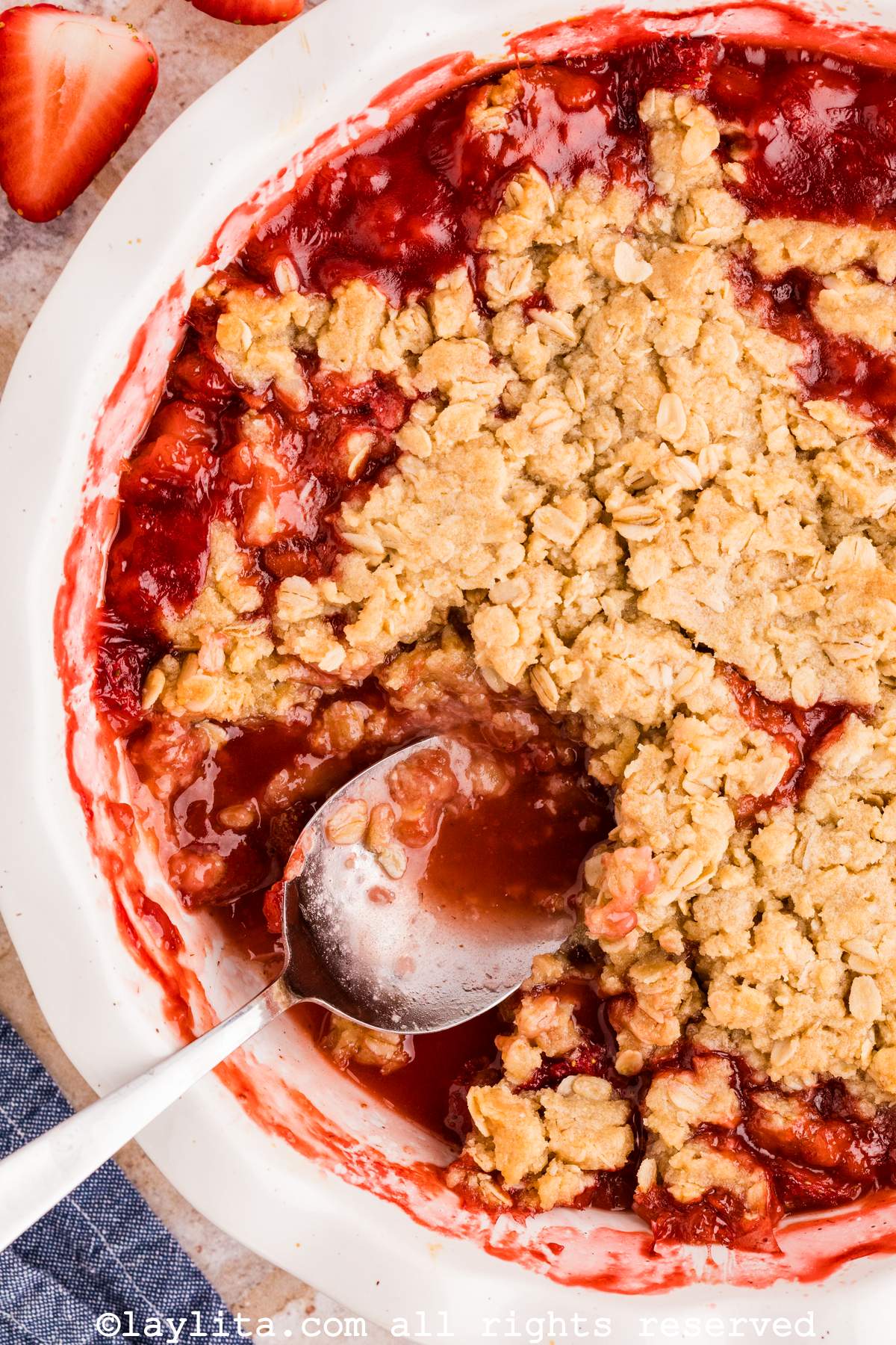 Closeup of a white baking dish full of strawbery crisp with a spoon in it