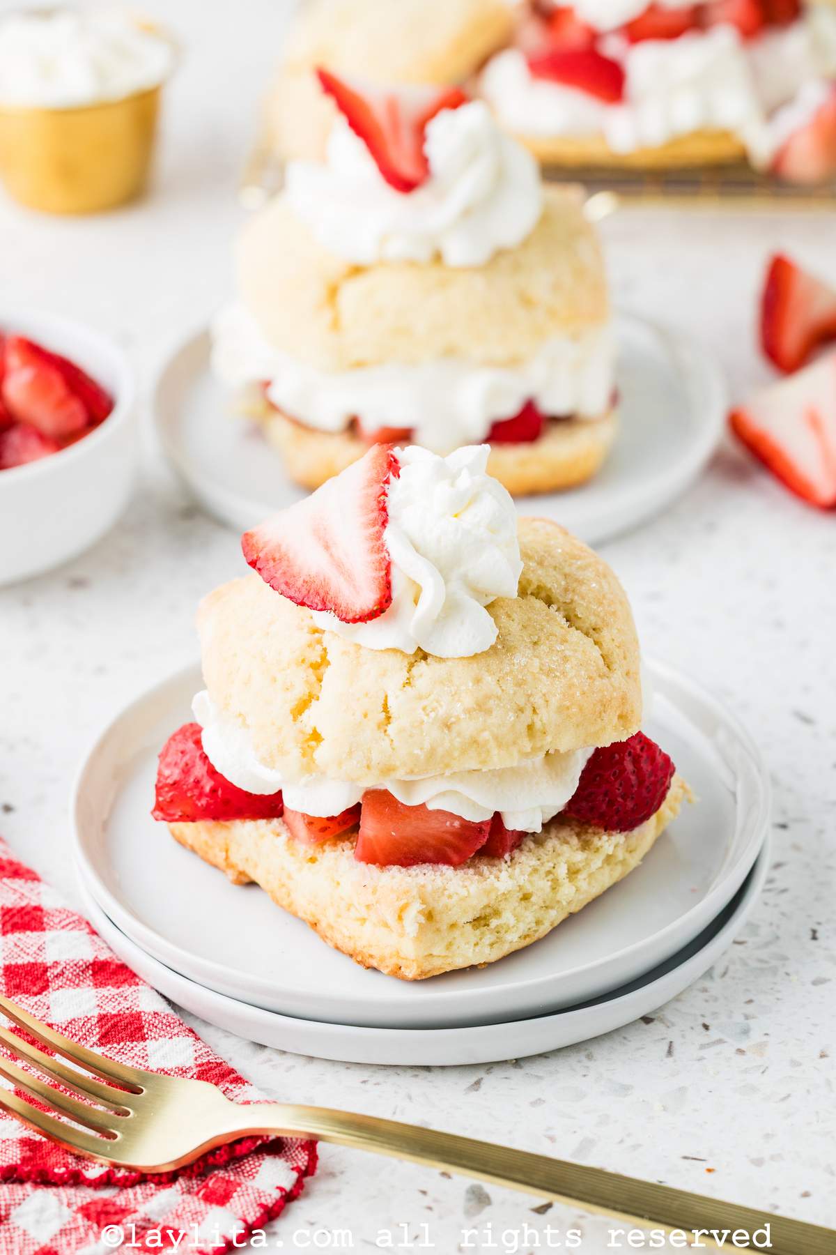 Two plates of strawberry shortcakes lined up, both garnished with strawberries and cream.