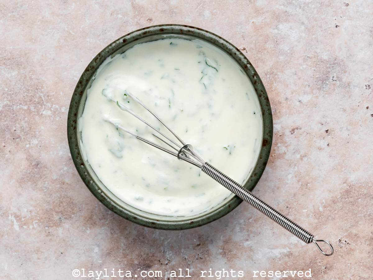 A bowl of mint lemon yogurt sauce with a small whisk in it