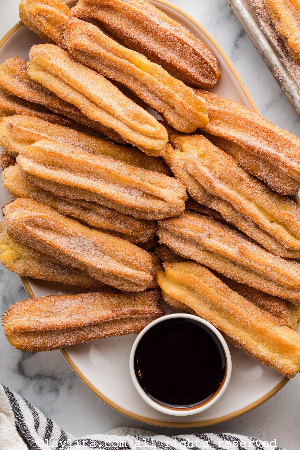 Several churrros topped with cinnamon sugar on a oval plate with a small bowl of chocolate sauce