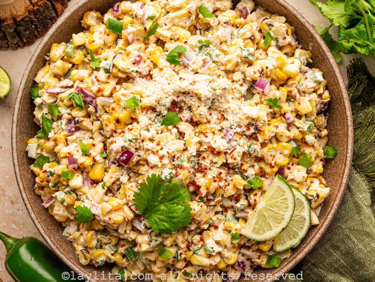 Closeup of Mexican Esquites or grilled street corn salad with cilantro leaves and lime slices on top