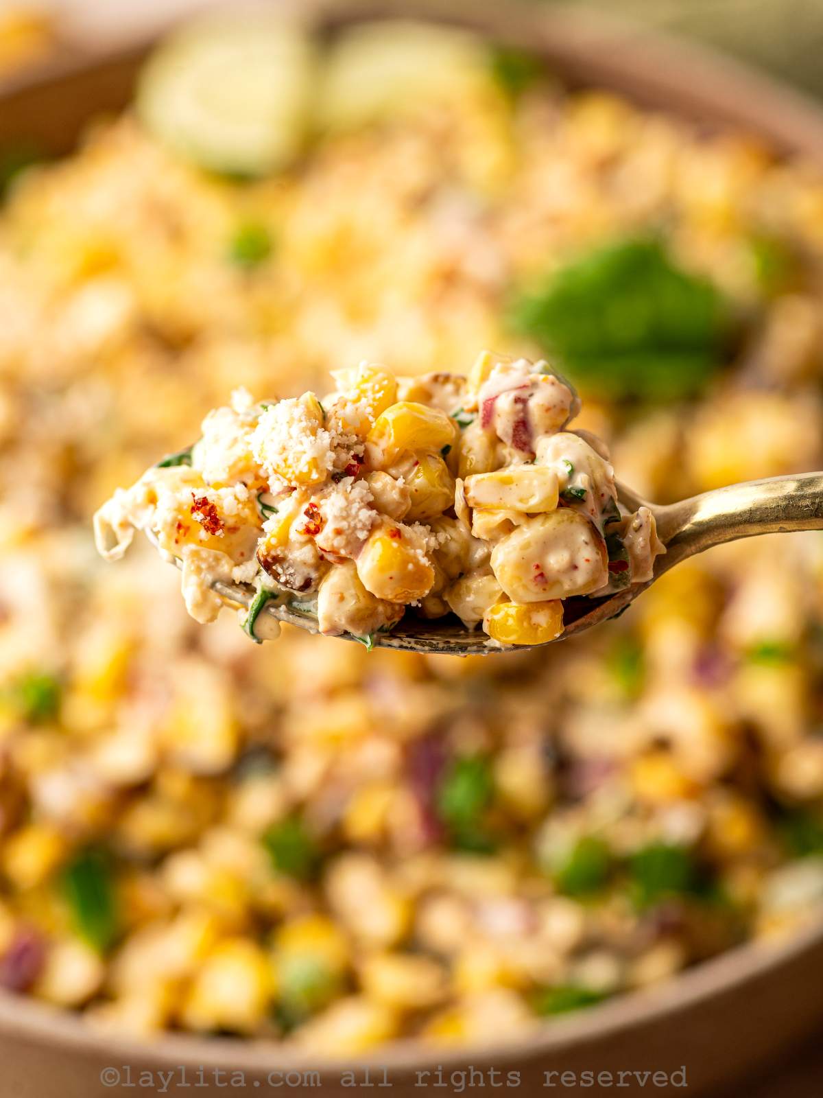 A spoon full of grilled corn salad with the rest of it blurred in the backgroun