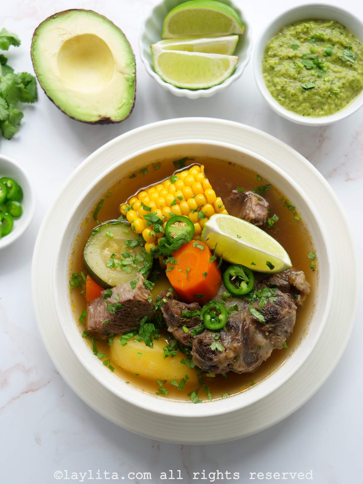 Overhead shot of caldo de res in a white bowl with lime and jalapeños on the side