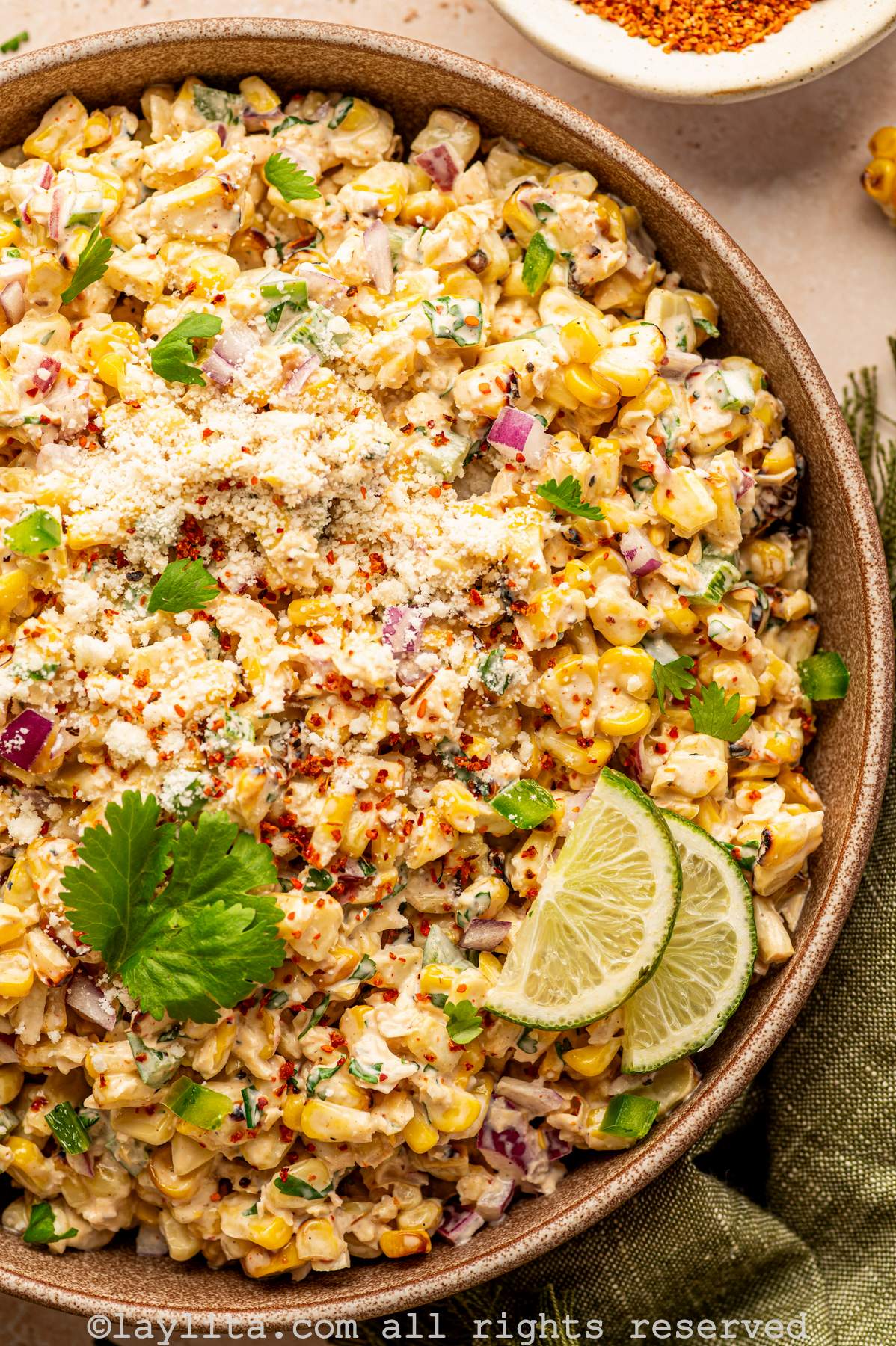 Close up of a bowl of grilled corn salad topped with crumbled cheese, diced red onions and cilantro