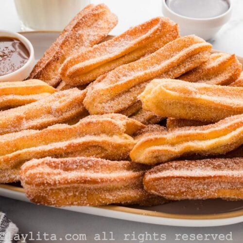 Sideview of a tray full of cinnamon sugar rolled churros, with a small bowl of caramel sauce on the side of the tray