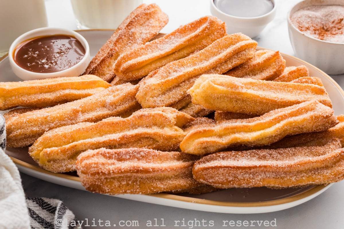 Sideview of a tray full of cinnamon sugar rolled churros, with a small bowl of caramel sauce on the side of the tray