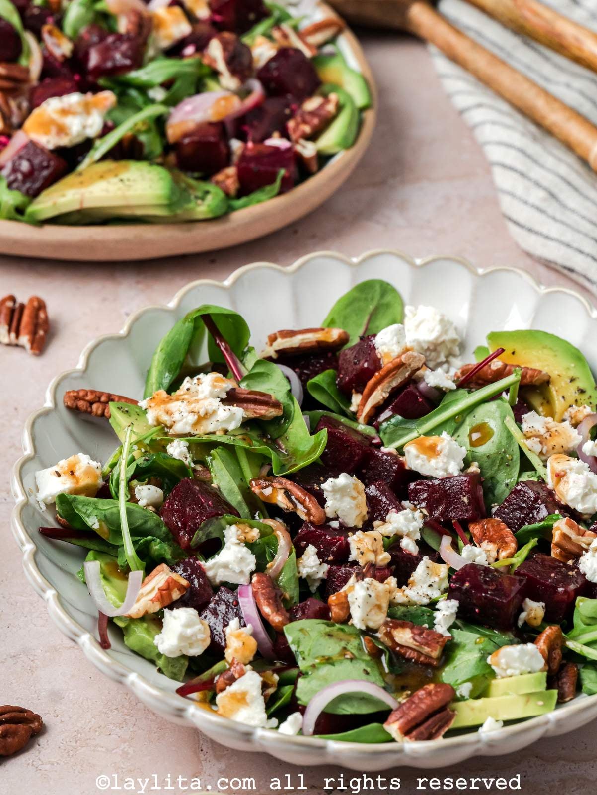 Beet salad with feta served in a bowl with the platter of salad in the background.