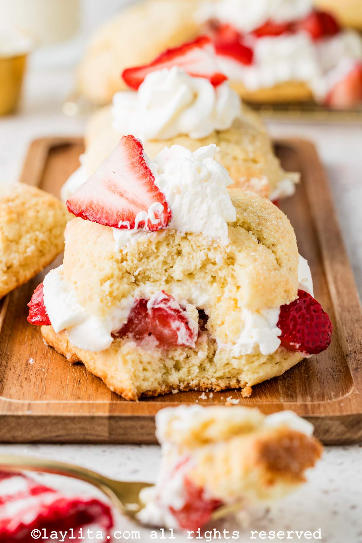 Two strawberry shortcakes on a wooden board with one of the missing a bite.