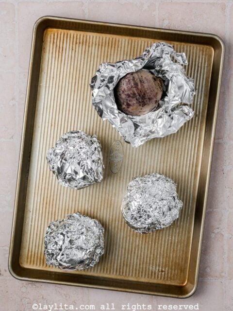 Beets wrapped in foil on a baking sheet