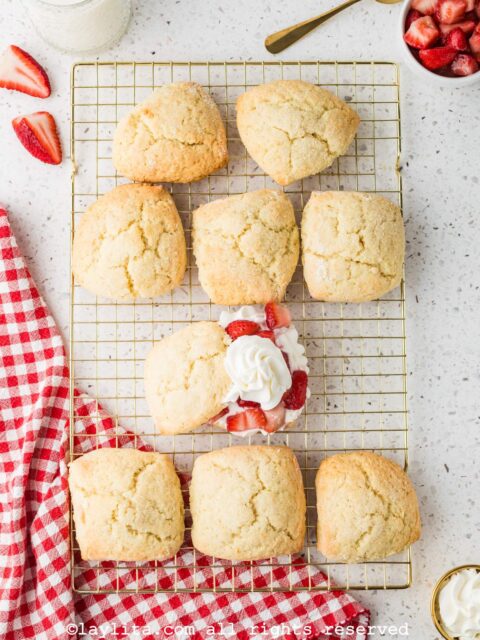 Overhead shot of a baking rack with several shortcake biscuits, with one of them cut in half and topped with strawberries and cream