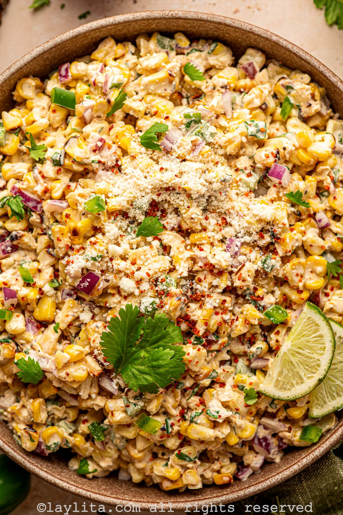 Overhead closeup view of Mexican Esquites or grilled street corn salad with cilantro leaves and lime slices on top