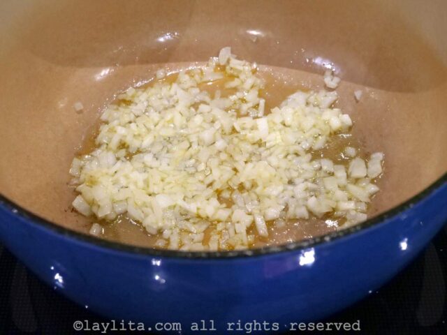 Diced white onions cooking in olive oil in a large cooking pot