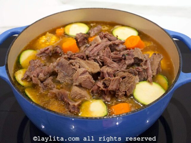 Chunks of cooked beef being added back to a pot of soup
