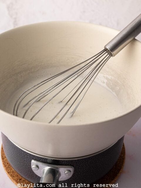 Egg whites and sugar being whisked in a heatproof bowl set over simmering water