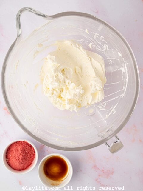Buttercream meringue in a glass bowl with strawberry powder and vanilla on the side