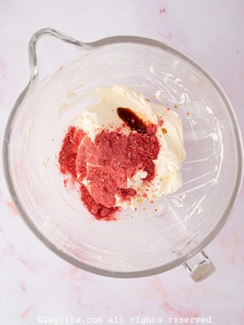 Aanilla extract and powdered freeze-dried strawberries being added to a bowl with buttercream frosting
