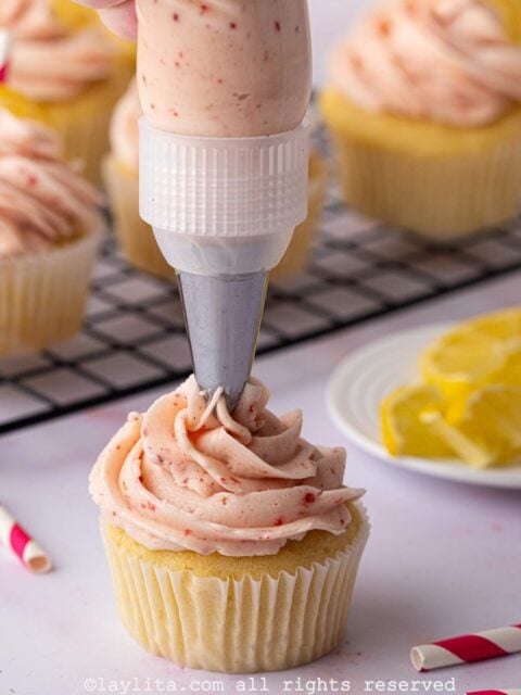 Strawberry buttercream frosting being piped onto a cupcake