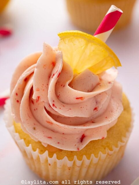 Closeup of a lemon cupcake decorated with strawberry frosting and decorated with a lemon slice and a striped straw