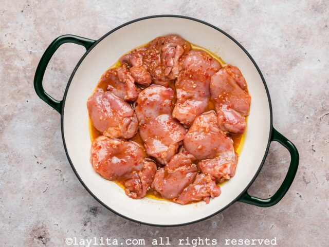 Raw harissa marinated chicken thighs cooking in a skillet