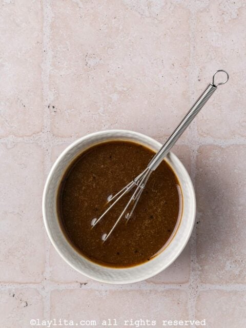 Balsamic vinaigrette dressing with mustard and maple syrup in a small bowl with a whisk in it