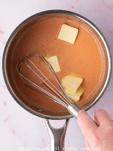 Cubes of butter being whisked into a pot of strawberry lemon curd