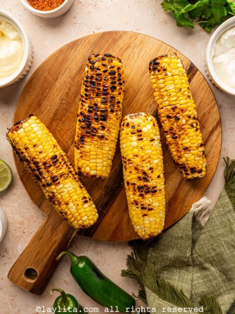 Four grilled ears of corn on a wooden board