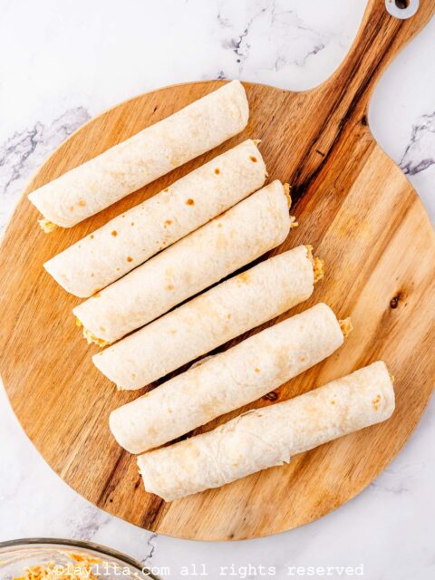 Tortillas rolled and filled with chicken and cheese on a wood board