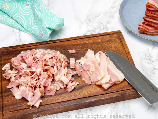 Ham and bacon being cut on a wood cutting board