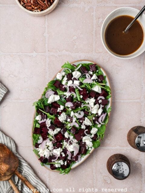 A platter with beet salad with feta cheese and shallots and a bowl of balsamic dressing on the side